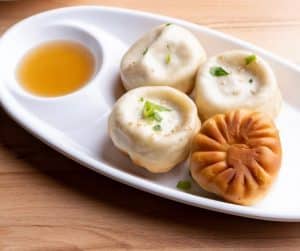 four fried dumplings on a white plate with dipping sauce at Bund Dumpling House
