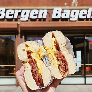 Person holding Bacon, egg, and cheese bagel in front of Bergen Bagel sign in Brooklyn, NY.